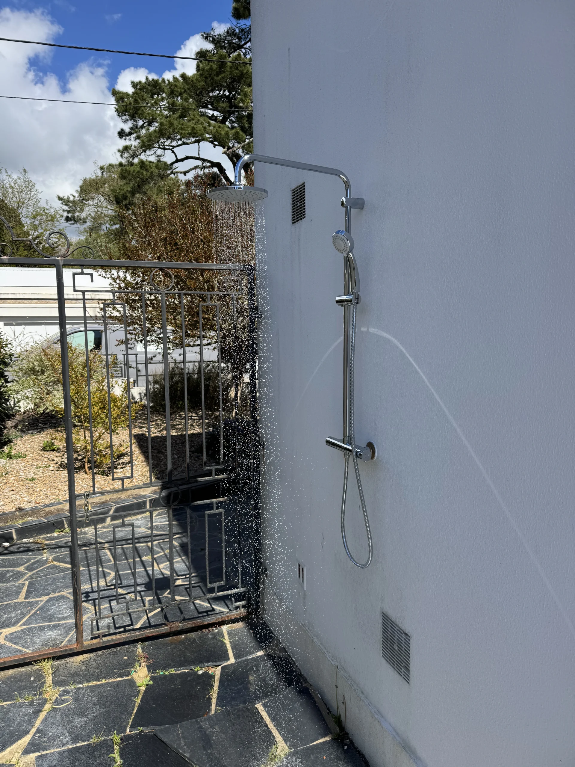 Douche extérieure chromée installée par Levesque Plomberie sur un mur de jardin, colonne avec pommeau pluie et mitigeur
