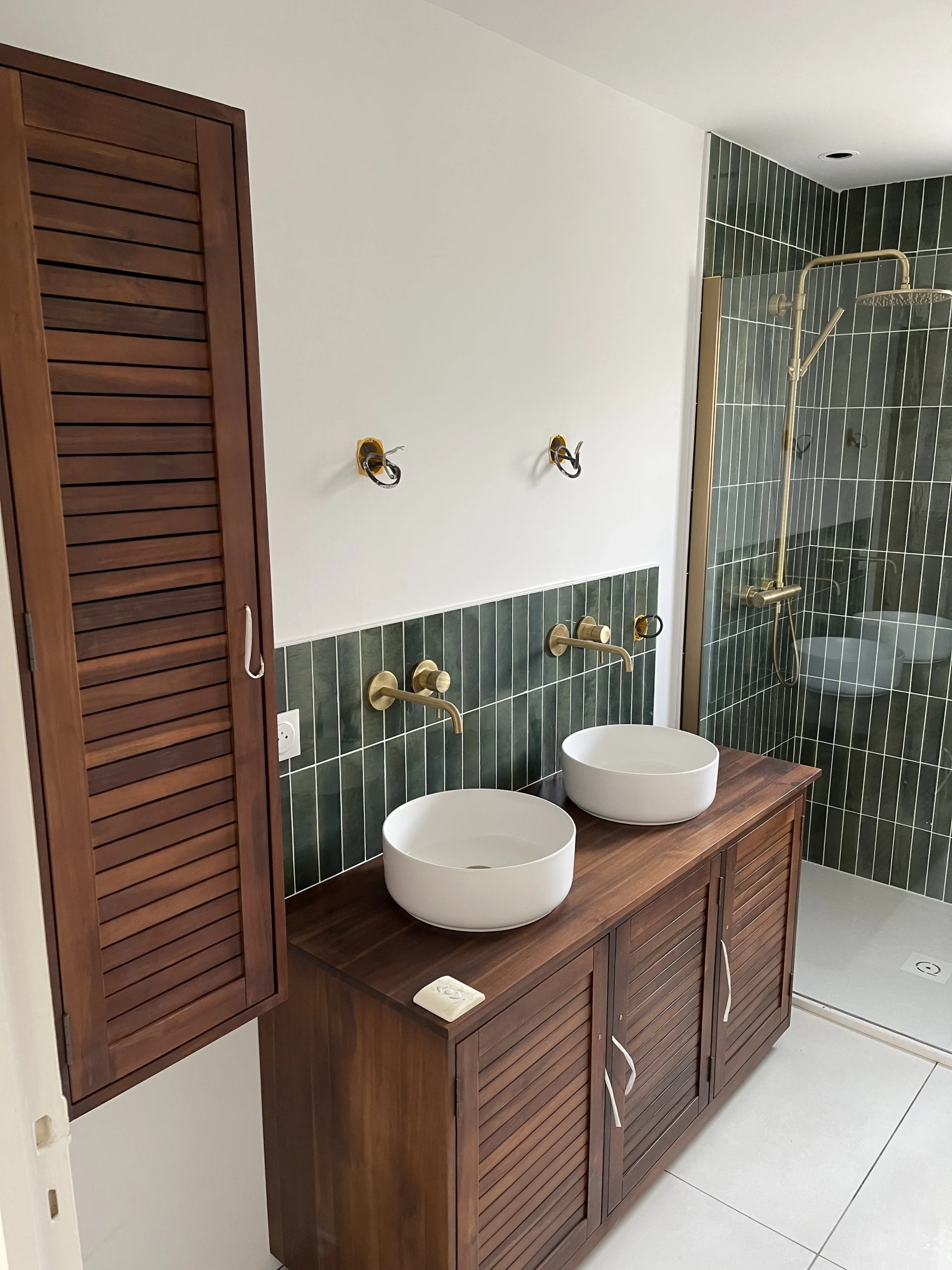Salle de bain rénovée par Levesque Plomberie : double vasque sur meuble bois, robinetterie dorée et douche à l'italienne en faïence verte